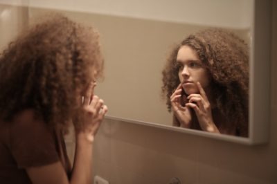 mulher olhando rosto com acne no espelho